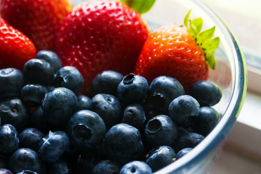 Close-up of fresh blueberries and strawberries in a glass bowl, showcasing vibrant colors and healthy appeal.
