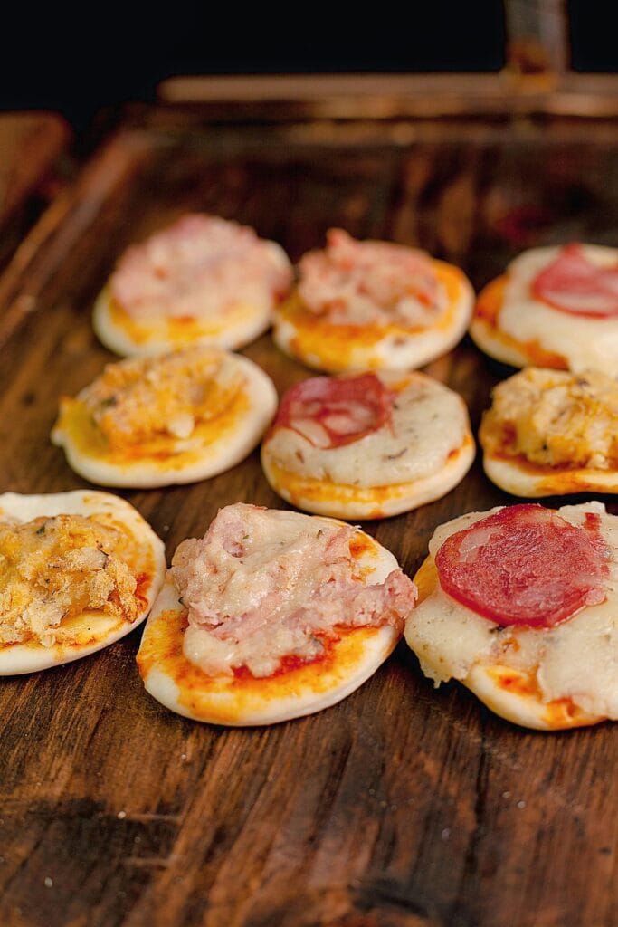 Tasty assortment of mini pizzas with cheese and toppings on a rustic wooden table, perfect for snacks.