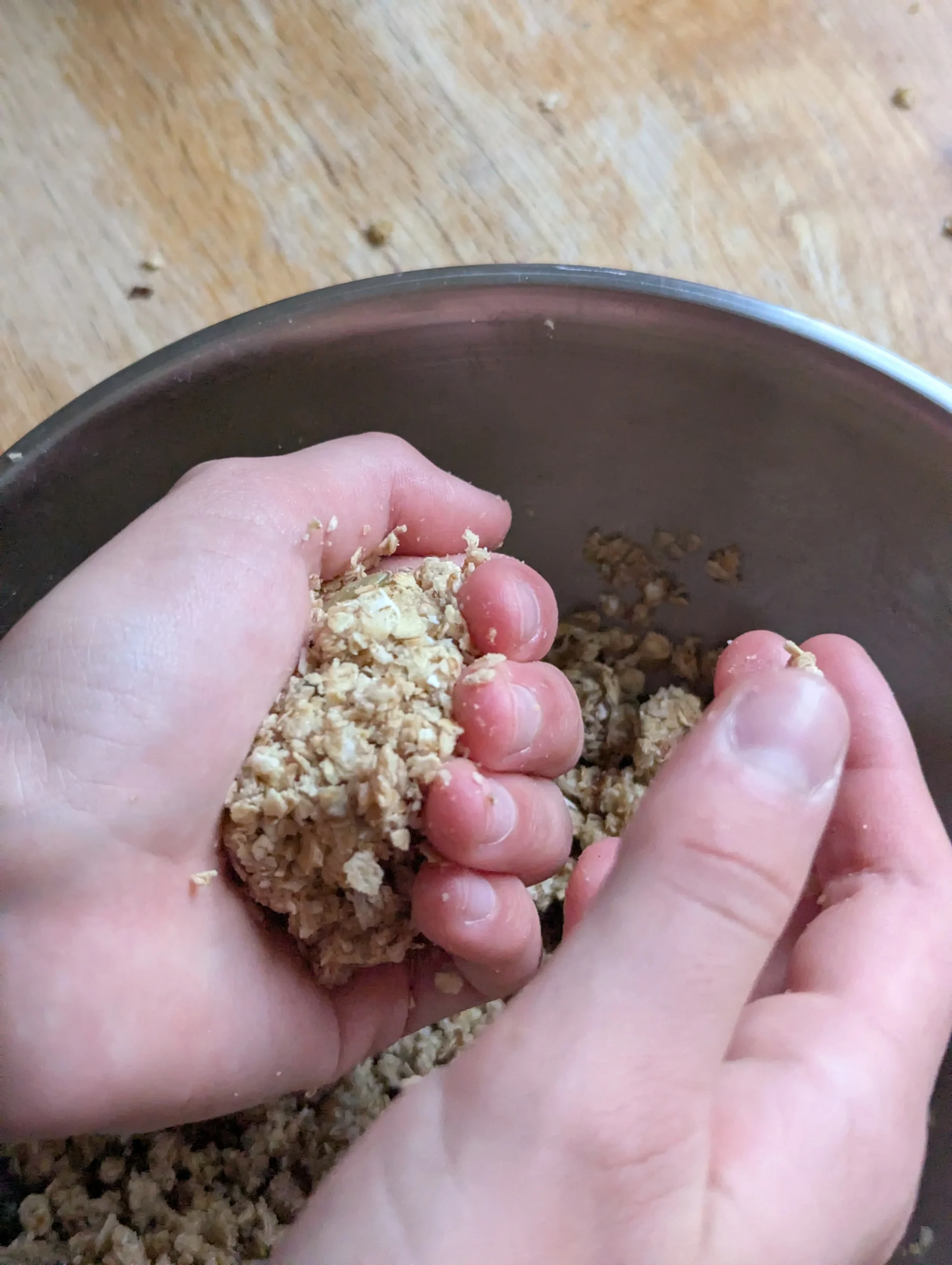 Child's hands rolling energy ball mixture with bits of oat and seeds visible