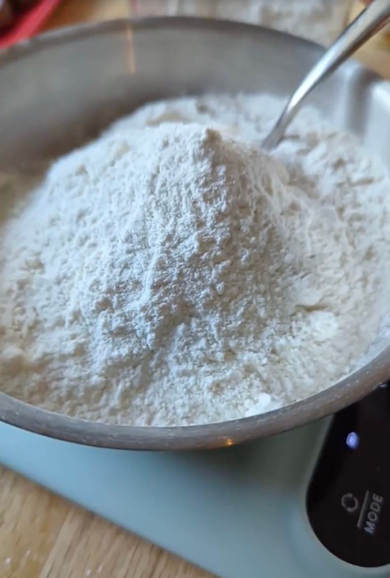 Child measuring flour into a mixing bowl at the kitchen counter