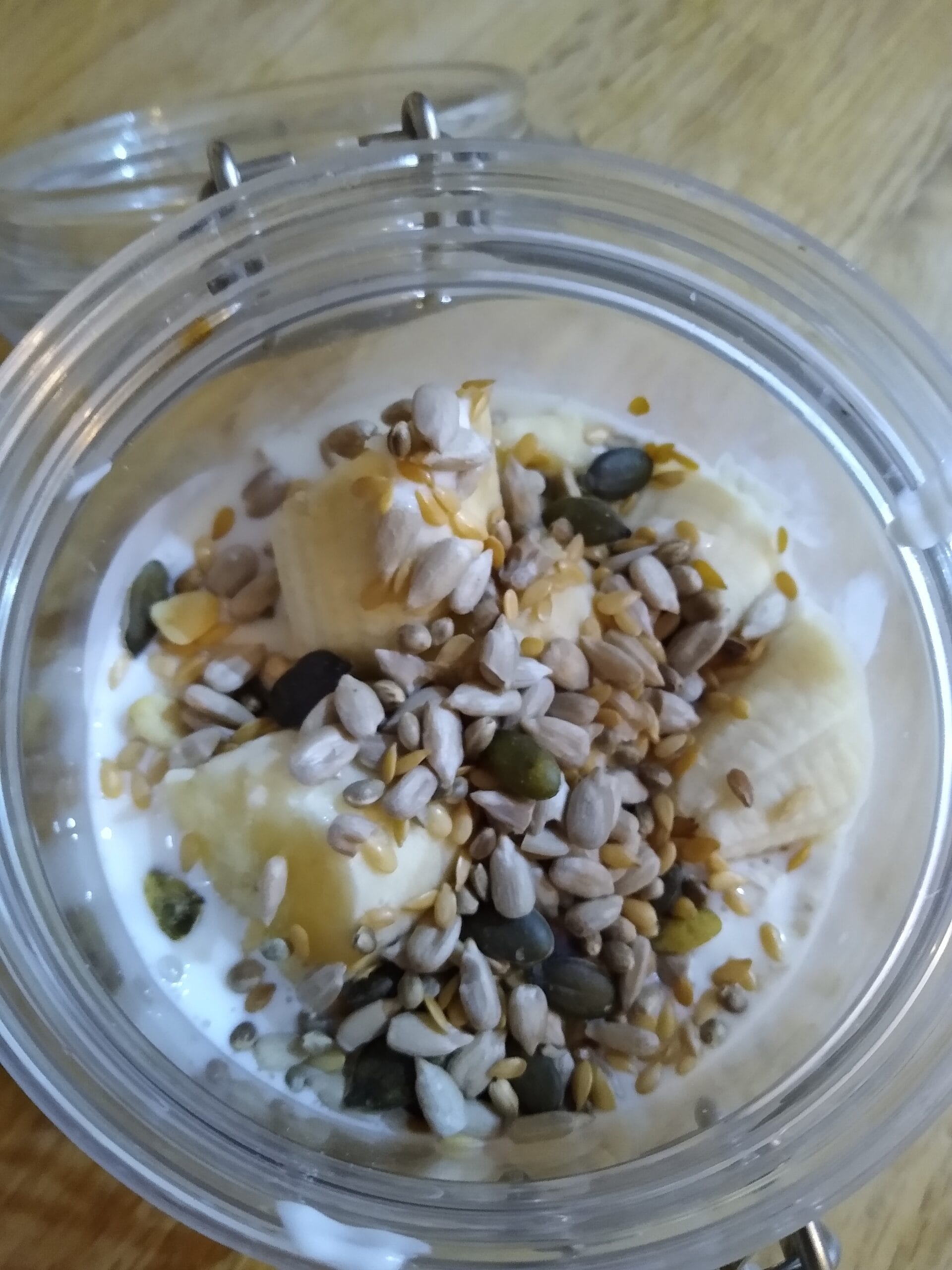 Layered breakfast in a tub with banana, seeds and yoghurt — overnight oats for children to make