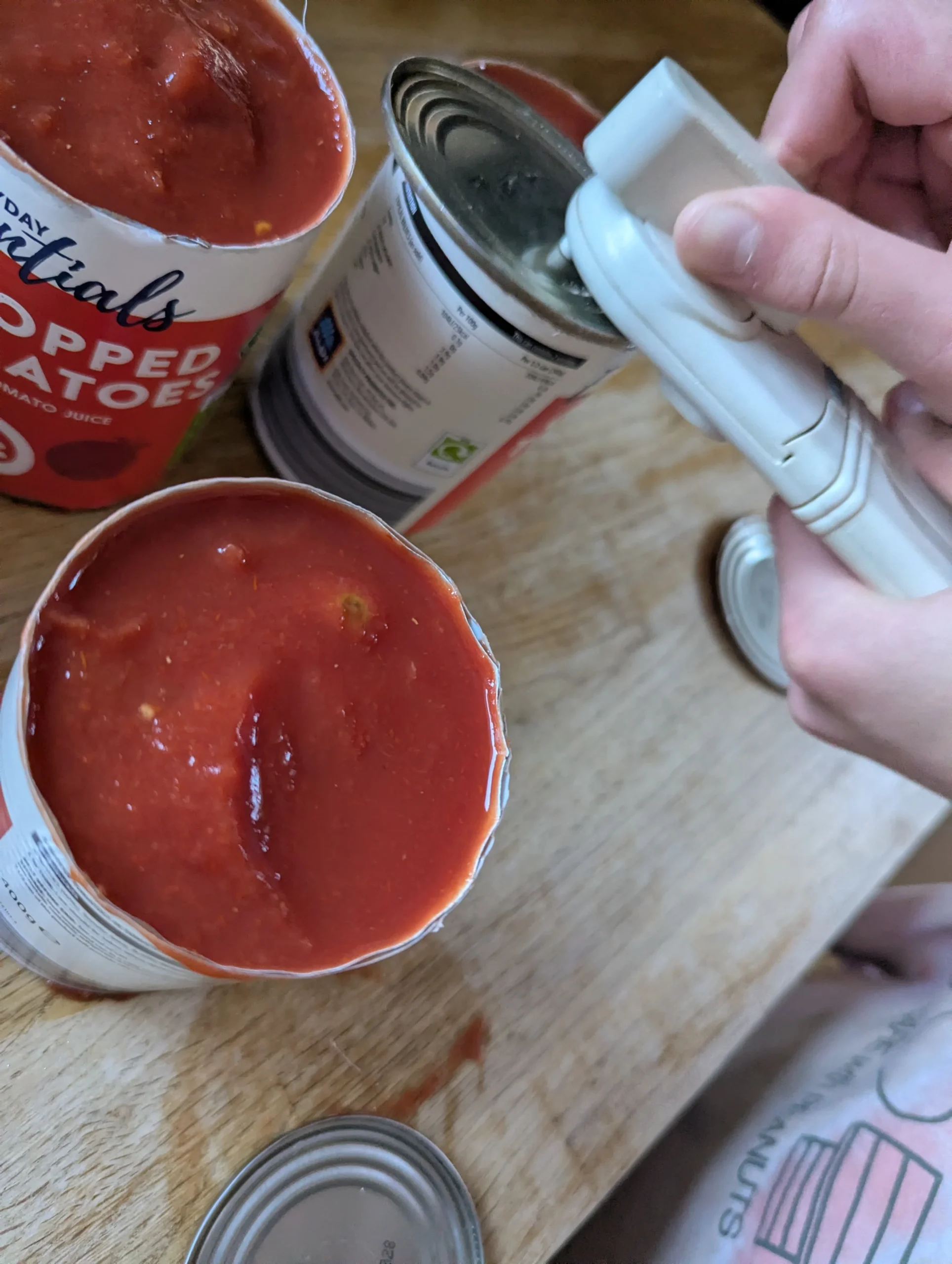 Child's hands using a manual tin opener on a tin of chopped tomatoes